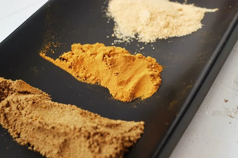 Black plate with small piles of the spices cumin, turmeric, and ginger.