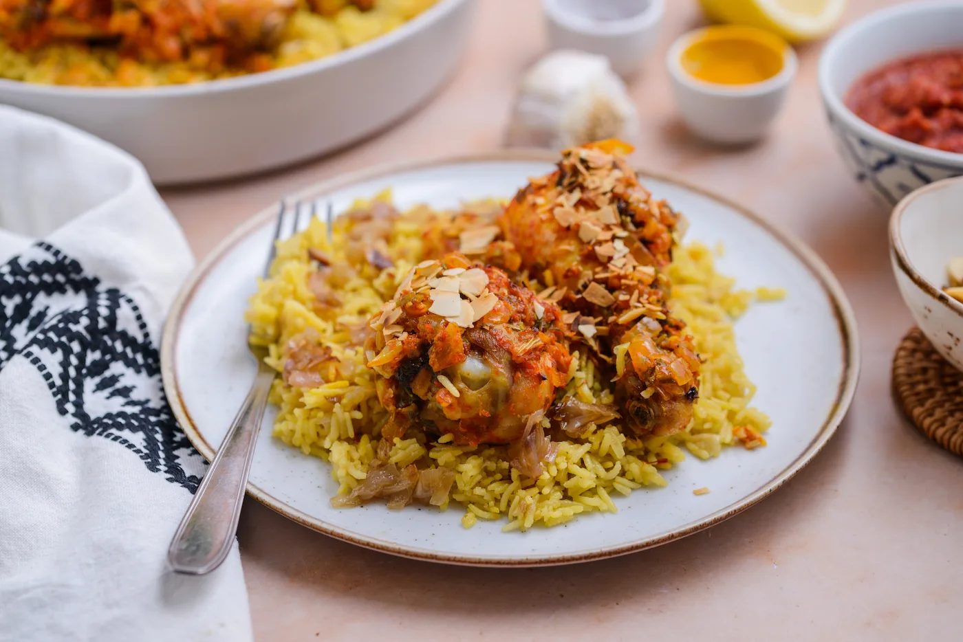 A white plate of yellow rice is topped with harissa baked chicken.
