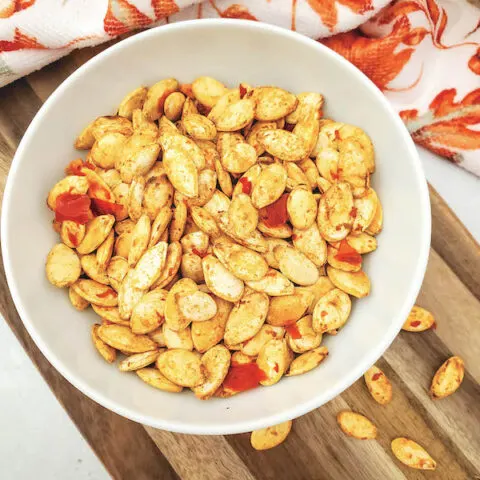 White bowl on a cutting board with roasted pumpkin seeds