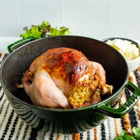 A cooked chicken sitting in a green roasting pot.