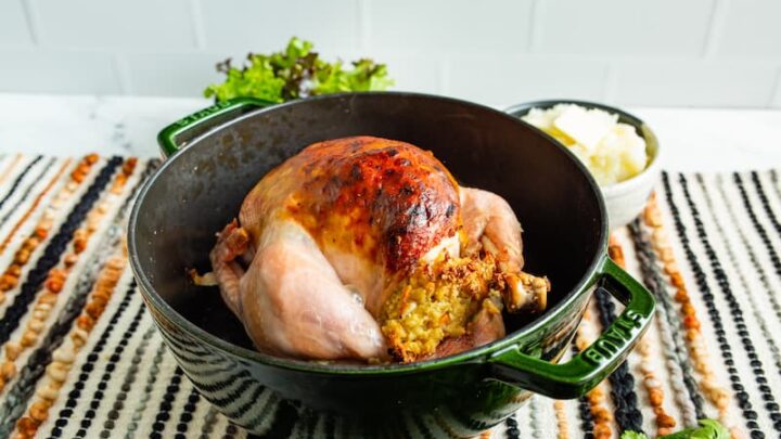 A cooked chicken sitting in a green roasting pot.