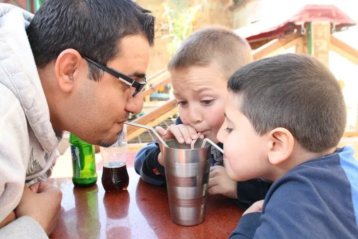 Dad and two kids drink from a metal cup with straws