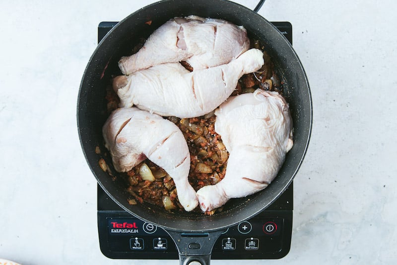 Chicken pieces are in a pot being cooked. They are sliced horizontally to absorb spices.