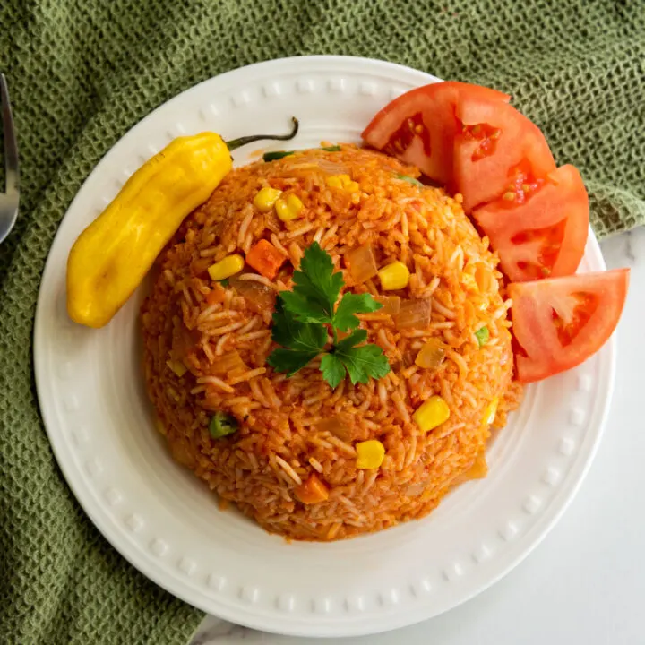 Plated jollof rice with a pepper and tomatoes