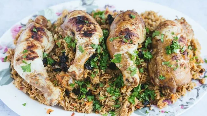 A large white platter is arranged with rice and chicken. The chicken kabsa is ready to be served.