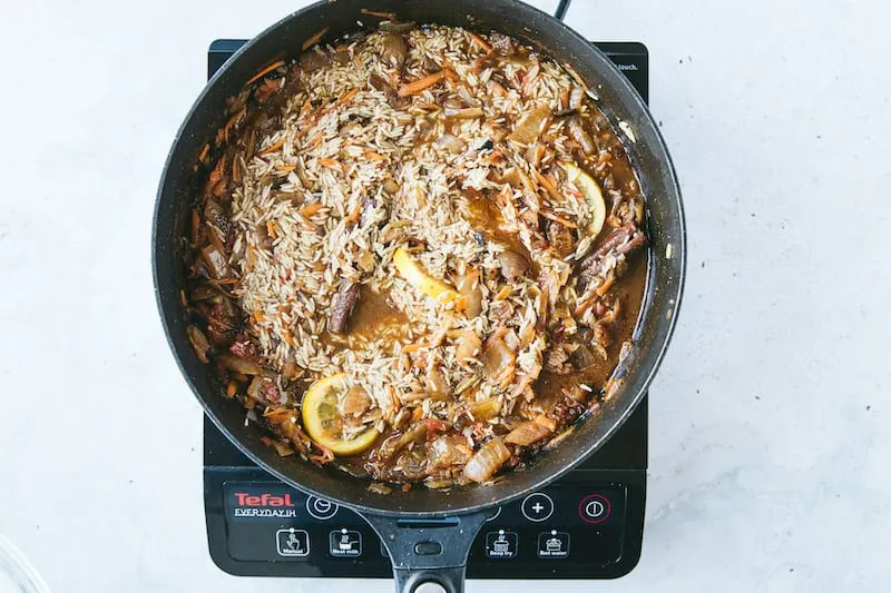 A skillet is on a burner with rice and chicken cooking for kabsa.