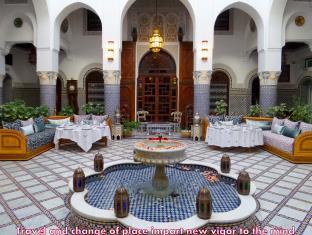 A white tile courtyard with arched walls in the background. A small fountain is in the foreground. 