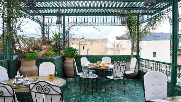 The covered rooftop of this Fez riad has green tile floors and several tables and chairs set for guests.