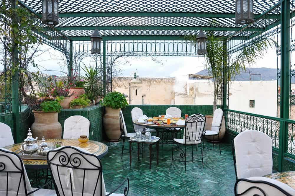 The covered rooftop of this Fez riad has green tile floors and several tables and chairs set for guests.