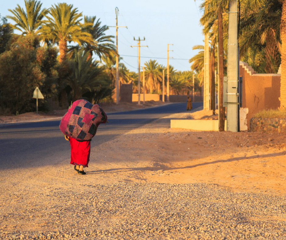 Moroccan woman in a long red djallaba walks with a bag over her shoulder