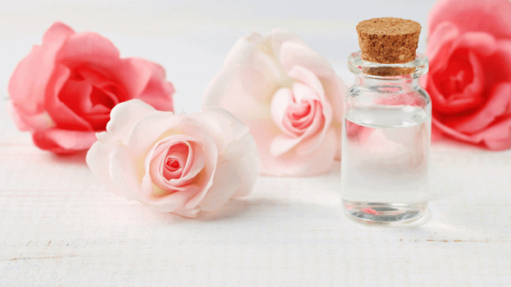 Vial of Rose Water with 4 pink roses behind it.