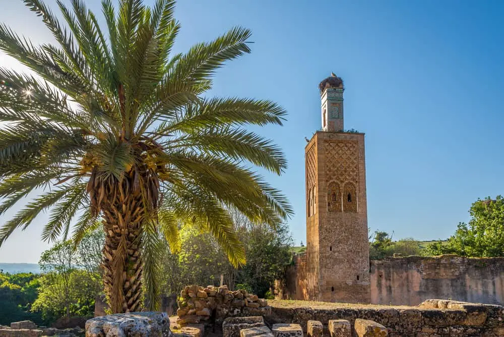 The Chellah ruins in Rabat against a blue background. The minaret structure is square and the most visible feature.