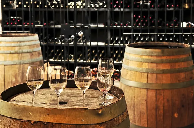 Three wine barrels are in the image with multiple full glasses of wine sitting on top of the barrel in the foreground.