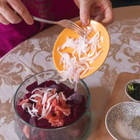 Adding sliced onions to a bowl of cooked beets.