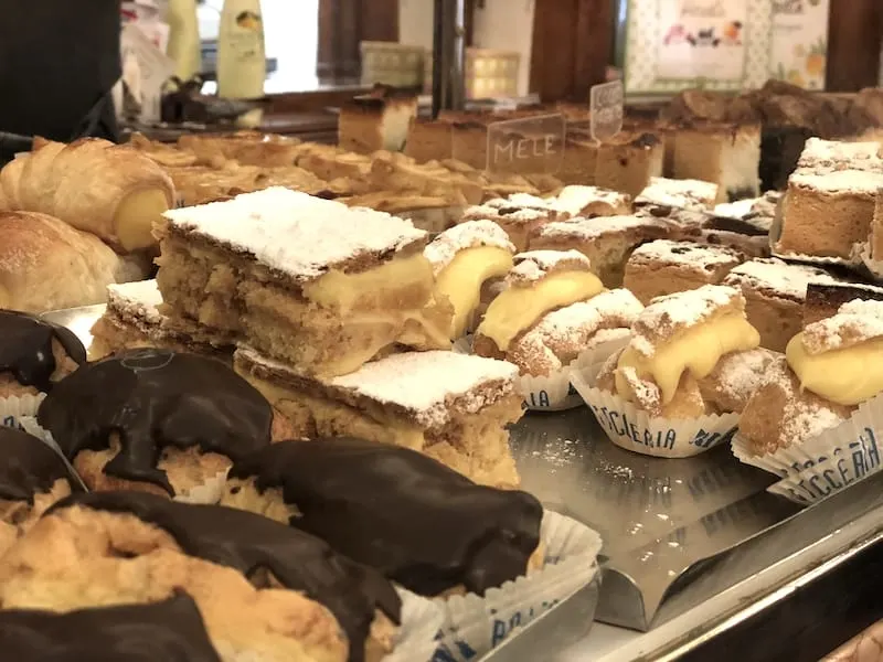 Bakery case with a variety of mixed Italian pastries including chocolate covered pastry, cream puffs, and cake slices.