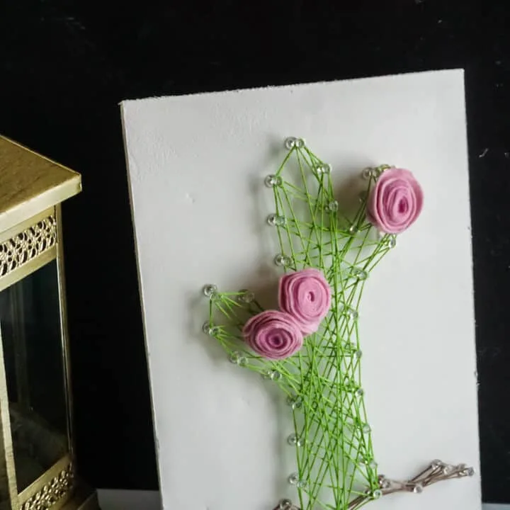 String Art Cactus Creation with Pink Roses. A lantern and string of beads are to the side of the craft.