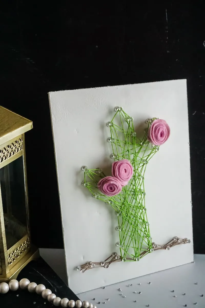 String Art Cactus Creation with Pink Roses. A lantern and string of beads are to the side of the craft.