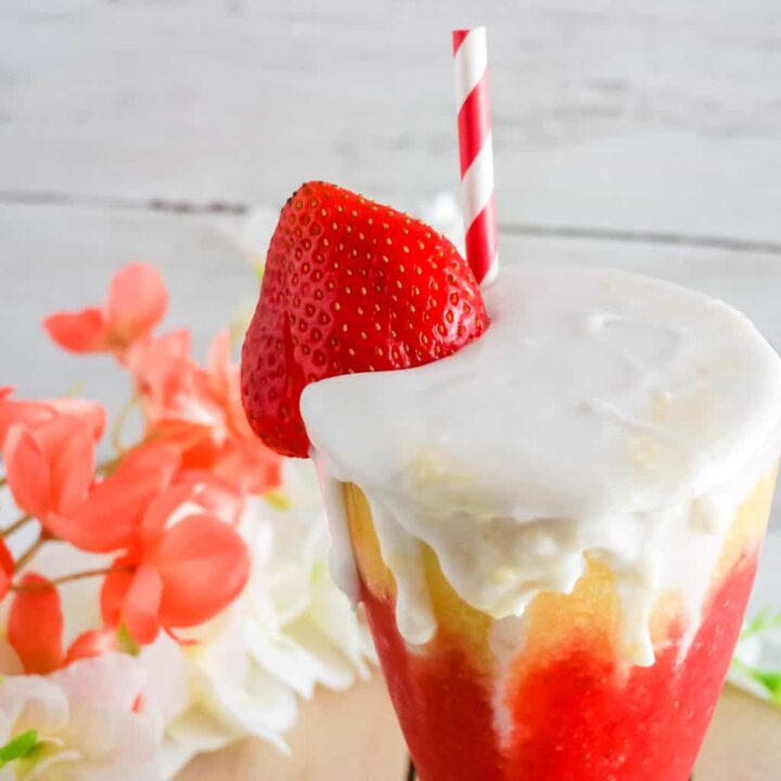 Half of a glass with a red and white straw, whipped cream and layers of pineapple and strawberry puree.