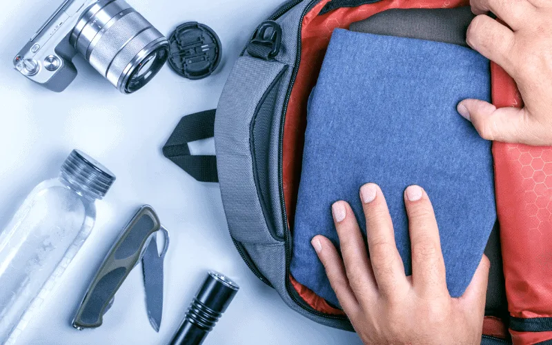 Open grey backpack with a camera, water bottle, and pen knife set off to the side. 