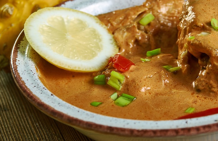 White bowl with a lemon slice and fish pieces in a red-orange curry sauce.