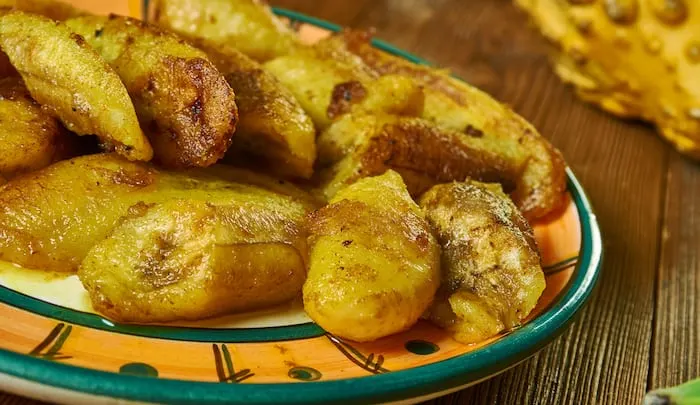 Plate on a wooden surface with fried plantain fritters.