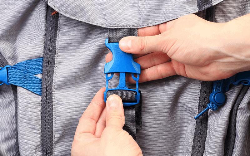 A grey backpack with blue snaps. Hands are snapping the middle snap.