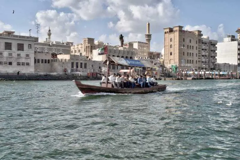 A traditional Abra boat goes down the Dubai Creek with buildings behind it