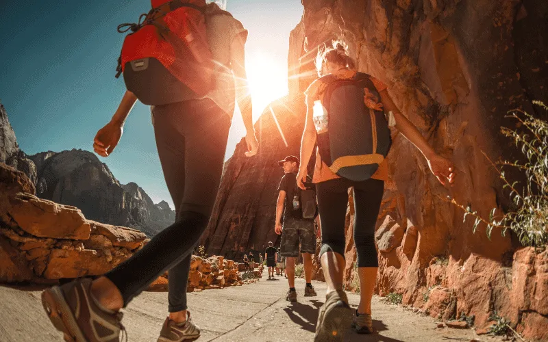 Three girls walk with sun shining and wearing backpacks.