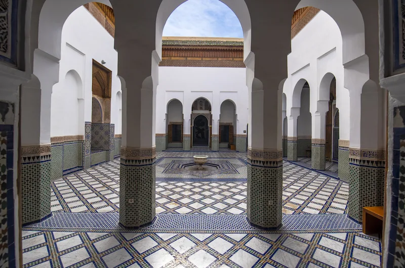 Courtyard of a Moroccan building with two white pillars in the foreground and blue and white tiled floor.