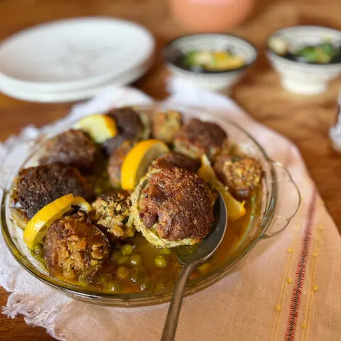 Meatball on a silver spoon with a glass plate behind it.