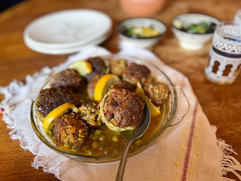 Meatball on a silver spoon with a glass plate behind it.