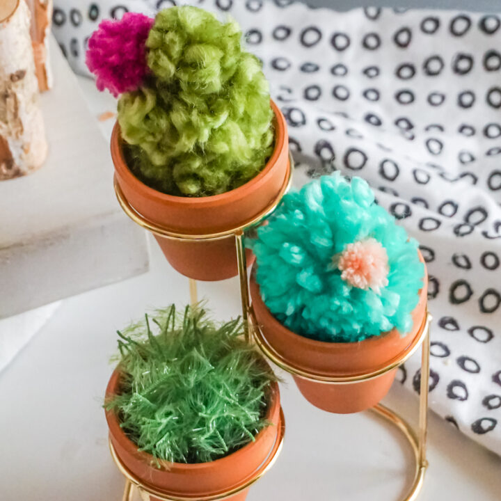 Terra cotta pots on a gold, tiered planter stand with pom pom cacti in each.