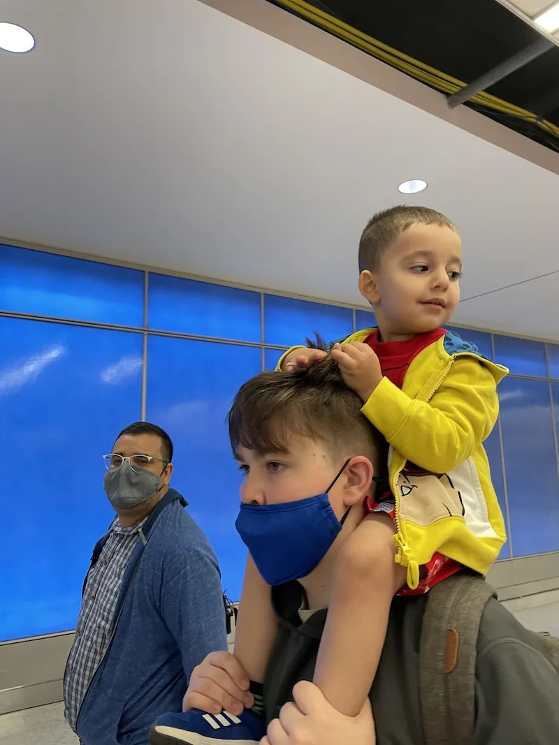 Toddler sitting on older brothers shoulders in an airport