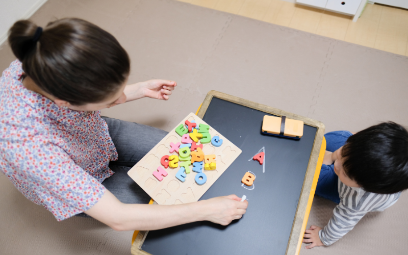 A woman and a child are sitting at a desk with English letters on the table