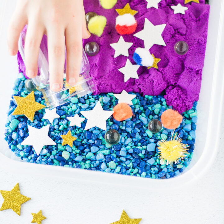 Childs hand in a bin with blue, purple and black colors and stars on top