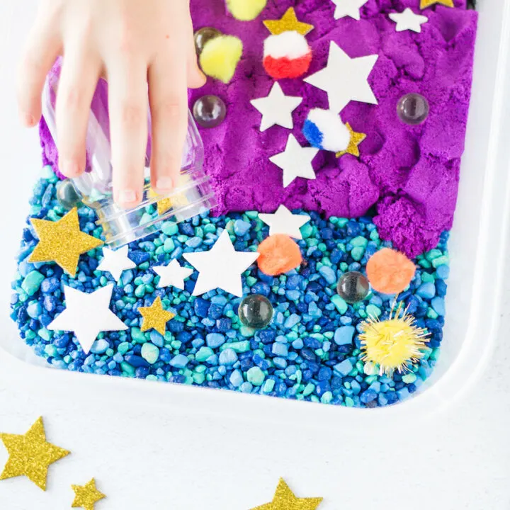 Childs hand in a bin with blue, purple and black colors and stars on top