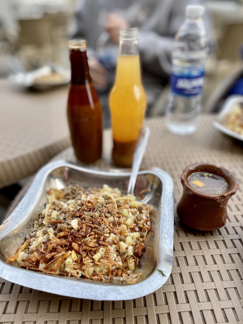 Metal plate with koshari and bottles of sauce