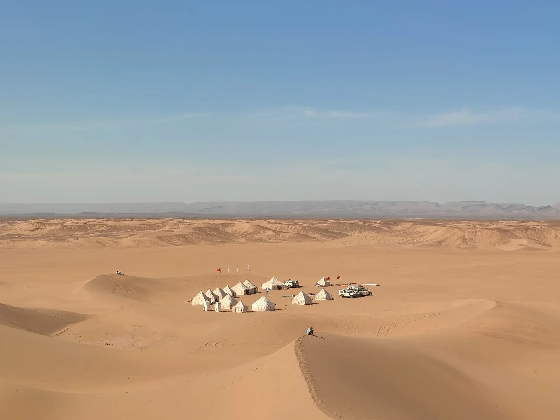 A Person Sitting on Sand Dune Near White Tents in Morocco