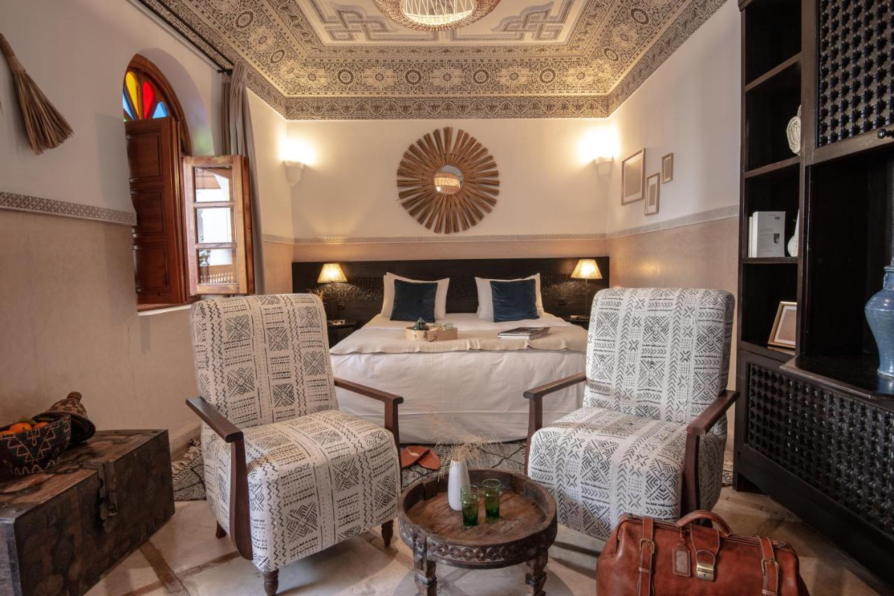 A suite at Riad Palais Calipau with white beddings, two armchairs and a bookshelf