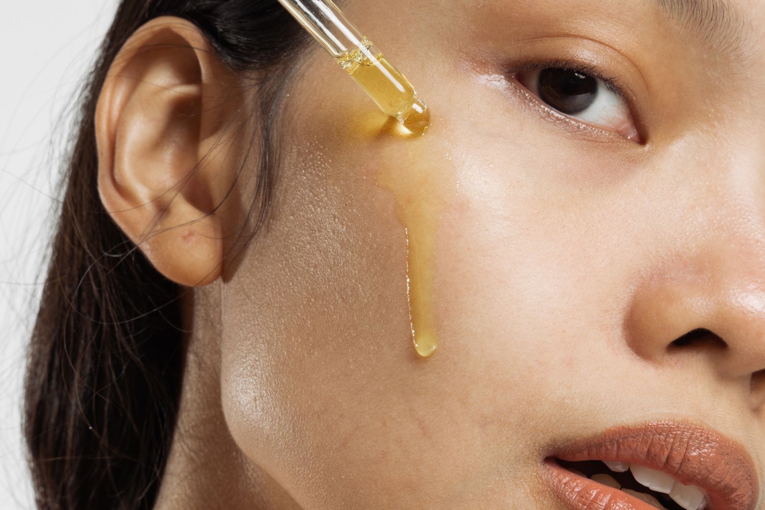 Closeup portrait of a woman applying Moroccan argan oil on face with a dropper