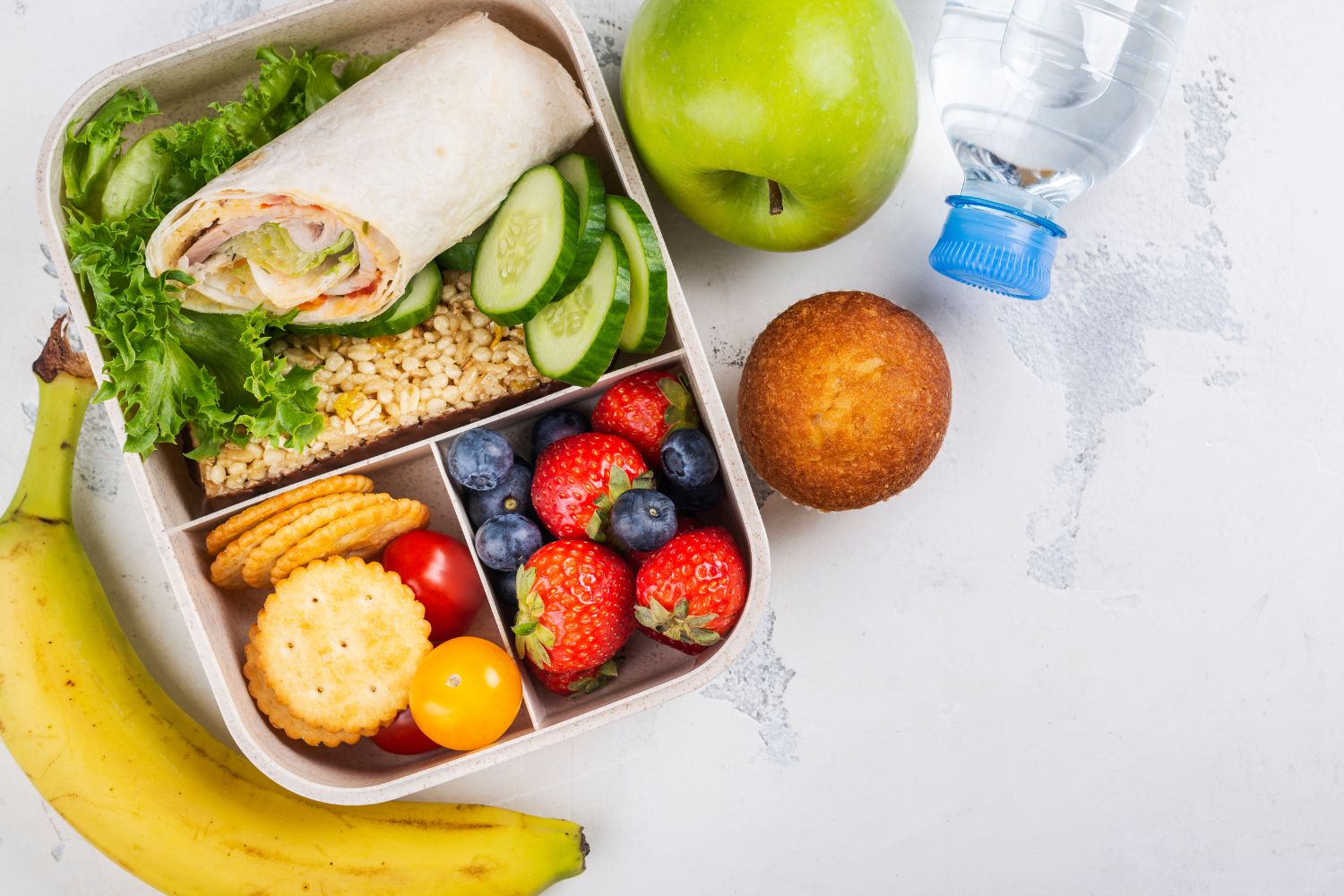 Healthy snack box for traveling with kids with roll, apple and muffin.